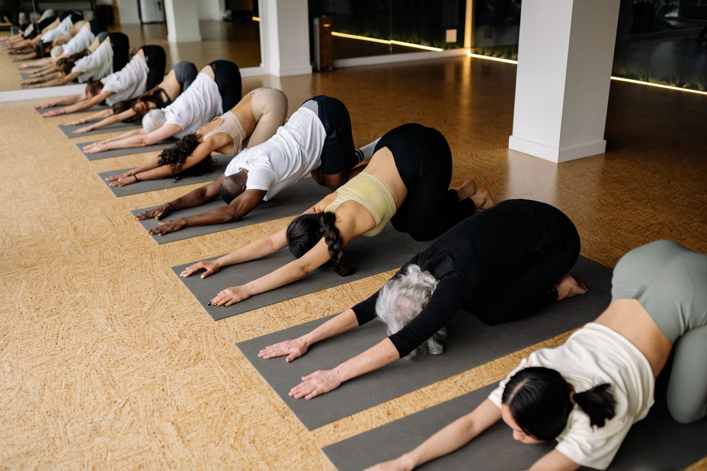A diverse group of people stretching on yoga mats in an indoor yoga class setting.